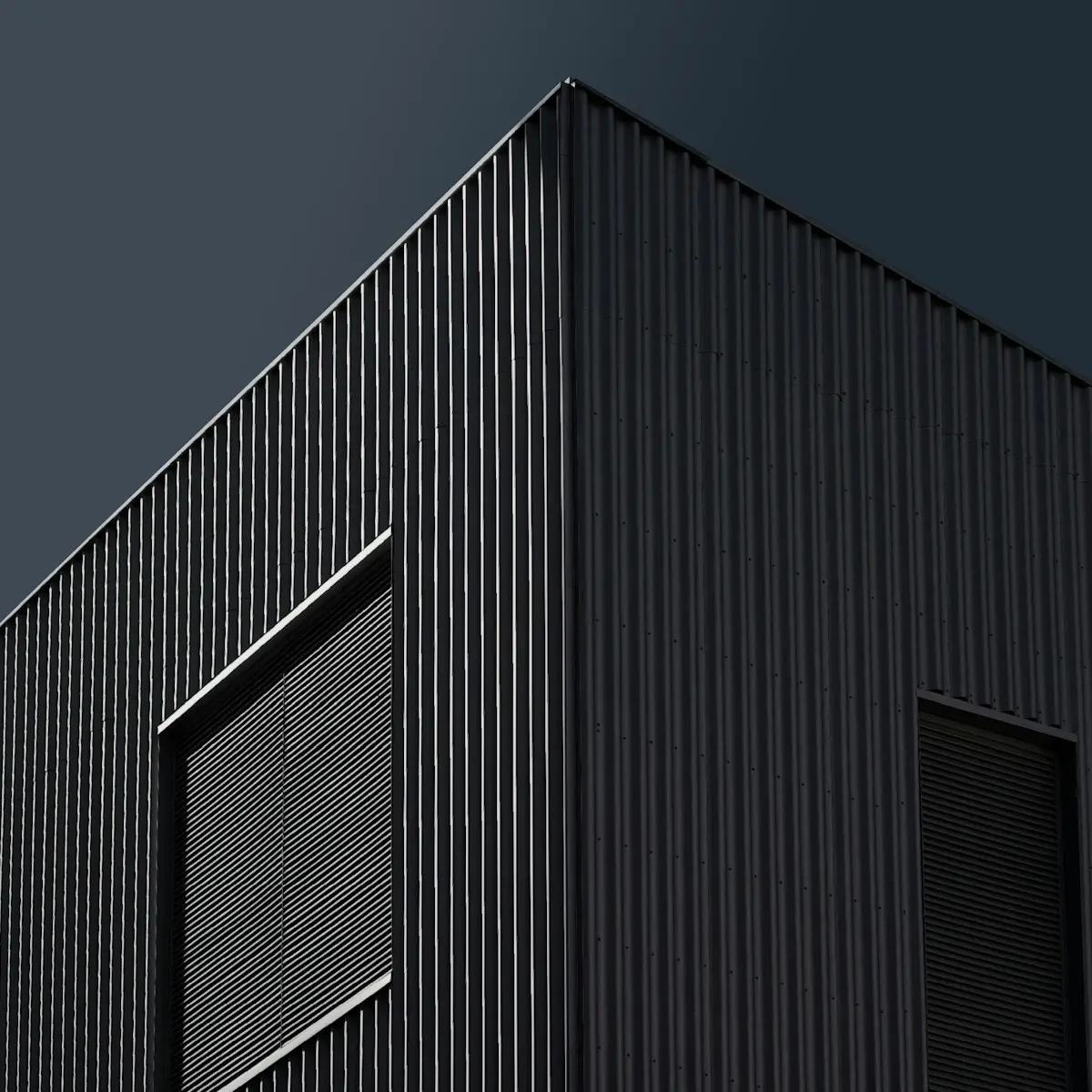 Black standing seam metal cladding on a building against a dark sky